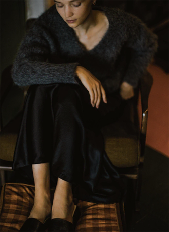 グレーVネックニット 39,600円／ソブ（フィルム）　黒サテンロングスカート 19,800円／ル フィル（LE PHIL NEWoMan 新宿店）　ピアス 14,080円／BRIE LEON（ジャック・オブ・オール・トレーズ プレスルーム）　スリッパサンダル毎日のように着るニット。その中のラインナップに欲しいのは特別感のある１着。とはいえ色やデザインではなく、ニットならではの甘さを演出してくれるふんわり感、肌感さえもアクセサリーのように。日常でドレスアップできるそんな１枚こそ、頼れるベーシックカラーで。