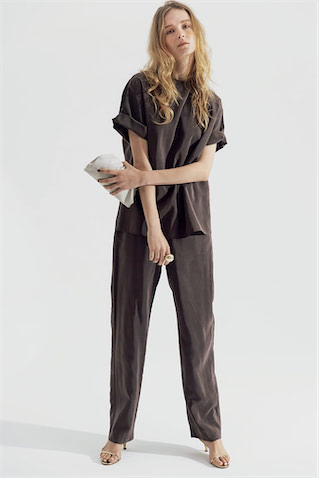 ハリのある質感を生かした そでのロールアップで立体感を ⚫︎ブラウンTシャツ 23,100円／ロエフ（エイチ ビューティ＆ユース）　ブラウンパンツ 29,700円／ロエフ（ユナイテッドアローズ 原宿本店）　リング 8,640円／アビステ　バッグ 17,600円／メゾン ヴァンサン、サンダル 50,600円／ネブローニ（ともにフラッパーズ）　モードに映るミニクラッチと華奢なサンダルに、最大の決め手はリング。「大ぶりを1つ」の潔さが強気をあと押し。